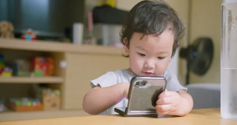 Child Using Mobile Phone Toddler Sitting At Wooden Table in Cute Toddler Home Stock Footage 332166270