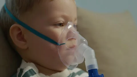Child using nebulizer for respiratory treatment on the couch at home Stock Footage 346706581