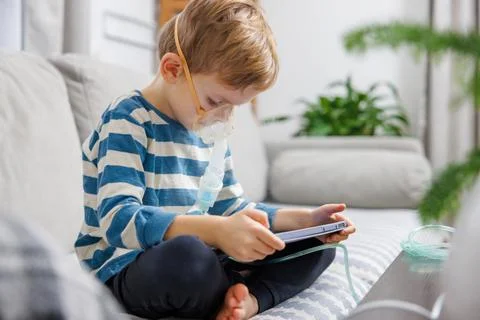 Child Using Nebulizer While Playing on Tablet at Home Stock Photos
