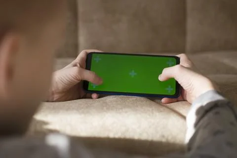 A child is using a phone with a chroma key screen mockup. Stock Photos