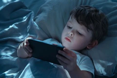 Child Using Smartphone in Bed Showing Gadget Addiction Stock Photos
