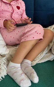 Child using smartphone at home in pink pajamas. Stock Photos