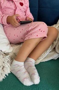 Child using smartphone at home in pink pajamas. Stock Photos