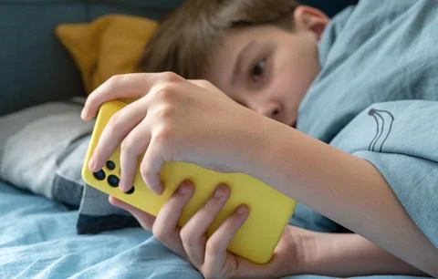 A child using a smartphone lying in bed late at night, playing games, watch.. Stock Photos