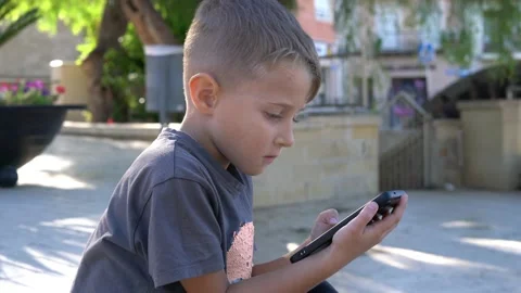 Child using smartphone outdoors focused on screen 스톡 동영상 328348337