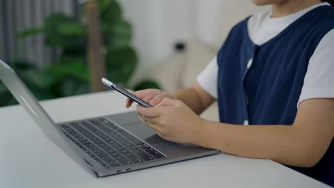 Child using smartphone while sitting at desk with laptop computer in modern.. Stock Footage 339377701