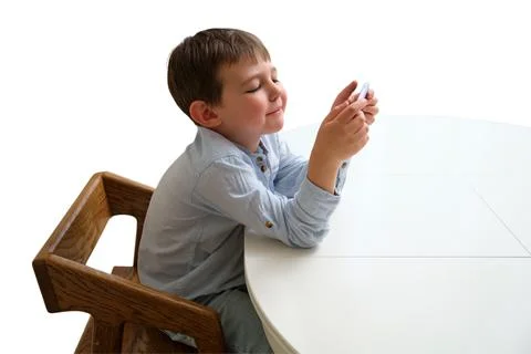 Child using smartphone while sitting at table on white background. Little b.. Stock Photos