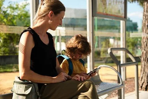 A Child using smartphone while waiting for school bus with mother Stock Photos