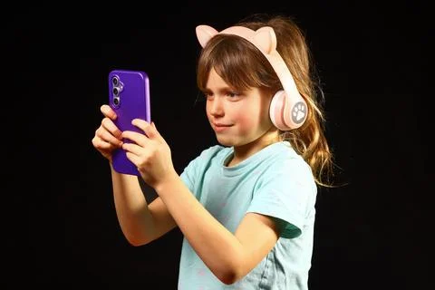 Child using smartphone while wearing pink cat‑ear headphones Stock Photos