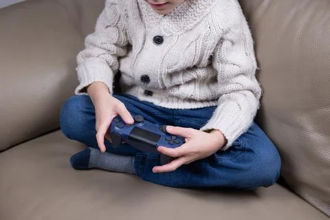 Child using technology. The boy sits on the couch, holds a game joystick and Stock Photos