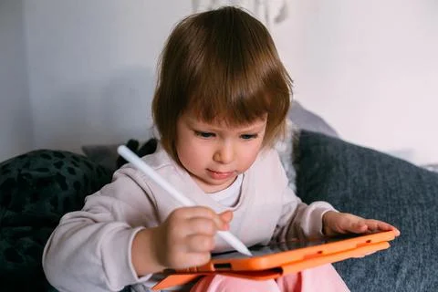 Child using technology. Toddler at home with a tablet and a pen stylus and draws Фото