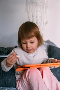 Child using technology. Toddler at home with a tablet and a pen stylus and draws Photos