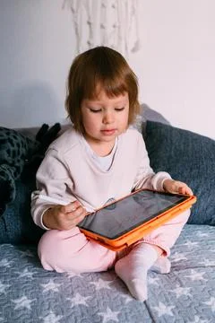 Child using technology. Toddler at home with a tablet and a pen stylus and draws 库存照片