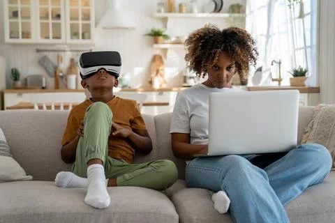 Child using virtual reality simulator headset while sitting on sofa with mother Stock-Fotos