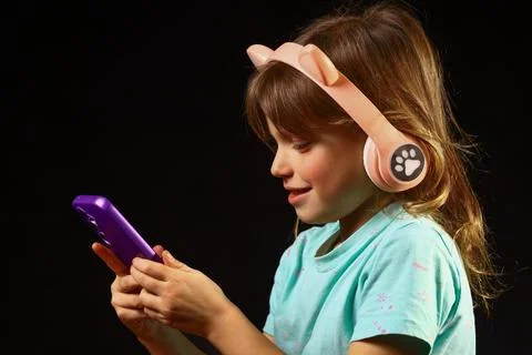 Child using a wireless smartphone while wearing playful cat‑ear headphones Foto stock