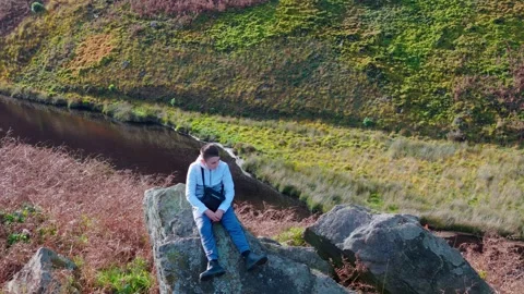 Child on vast boulder, lost in thought. Aerial video rotates gently around .. 库存影片 254160807