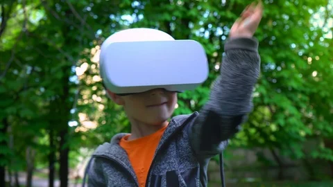 Child in VR glasses fighting off something in the summer park, child have fun Stock Footage 89140496