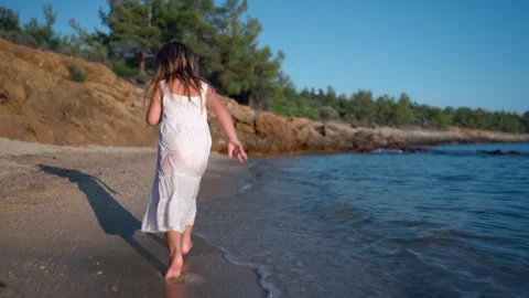 Child walking along the beach, splashing in the water Видео 341120421
