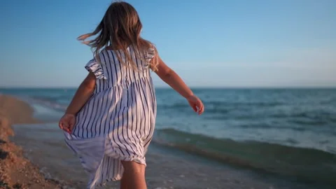 Child walking along the beach at sunset with gentle waves Видео 341119493