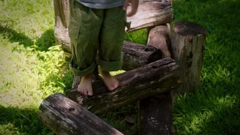 Child walking barefoot across a zigzag course of wooden logs in a sunny gra.. Stock Footage 346600651