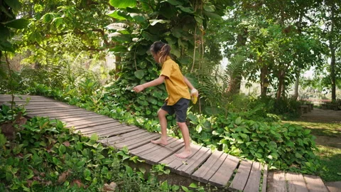 Child walking barefoot on wooden path through tropical forest Stock Footage 306728962