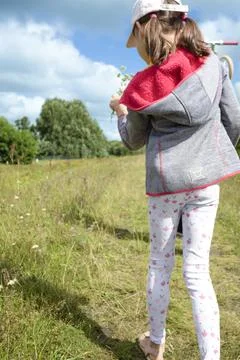Child walking in a grassy field while holding a plant under blue sky Stock-Fotos