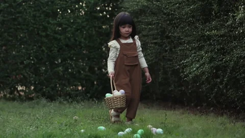 Child walking on green grass and carrying a basket during an Easter egg hunt Stock Footage 330950570