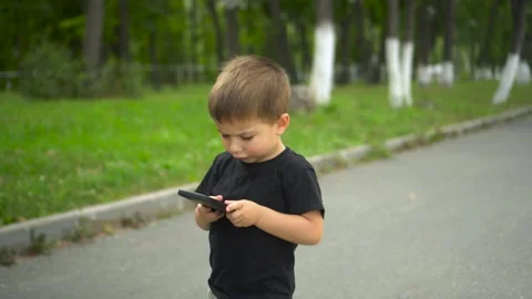 Child walking on park path smiling while holding smartphone 4k Stock Footage 322518404