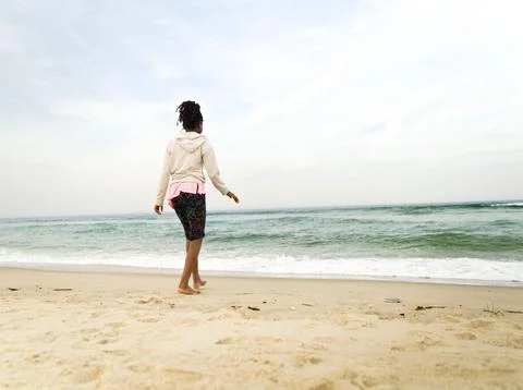 Child Walking on Sandy Beach Facing Ocean, Peaceful Coastal Scene Stock Photos