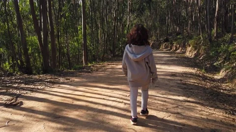 Child walking through a forest or a park with green leaves Stock Footage 134837317