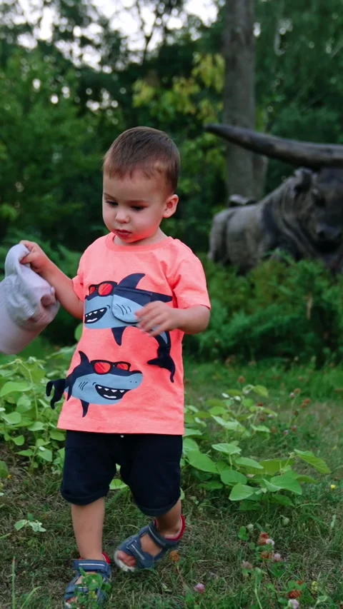 Child walks by the grass trying to get his cap. Kid comes up to camera, drops Stock Footage 337509297