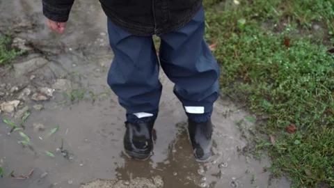 A child walks through a puddle in rubber boots and waterproof pants. Stock Footage 285618670