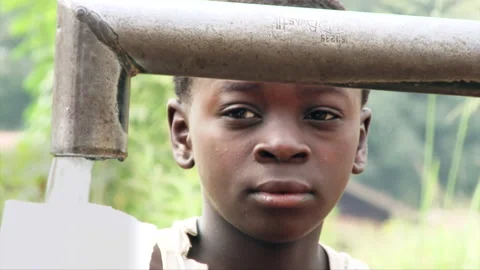 Child watching pumping water EXT Liberia Stock Footage 133924877