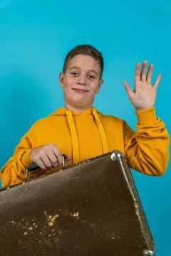 Child waves while holding a suitcase in front of a blue background Stock Photos