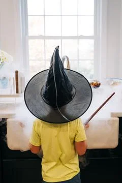 Child wearing witch hat casting magic spell in kitchen Stock Photos