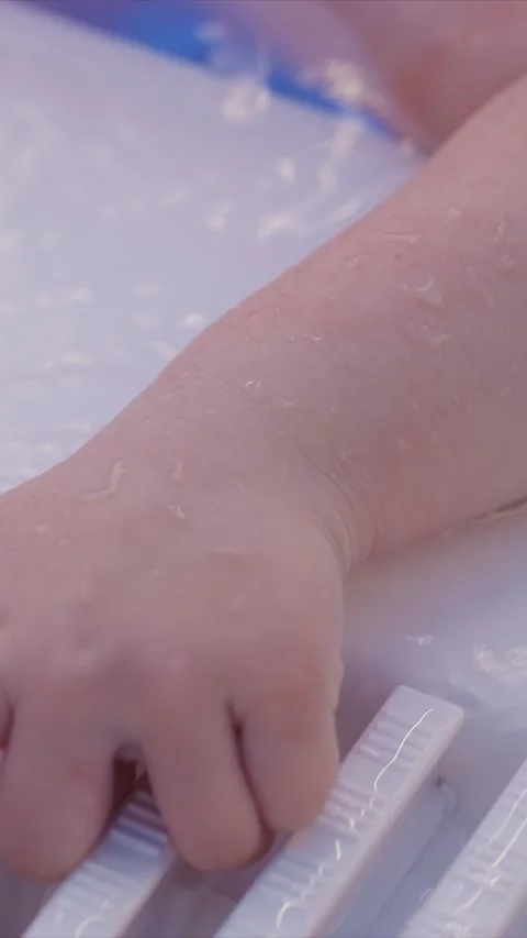 Child wet arm interacting with white plastic textured bars in water filled bath Stock Footage 342786703