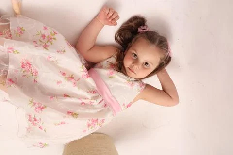 A child on a white background in an elegant light dress. Little girl lies on the Stock Photos