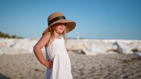 Child in White Dress Posing on Beach with Sun Hat Видео 341120437