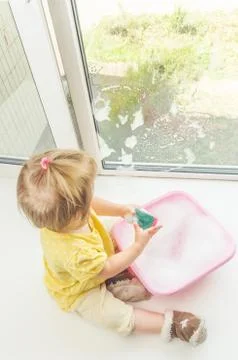 Child on the windowsill washes the window Stock-Fotos