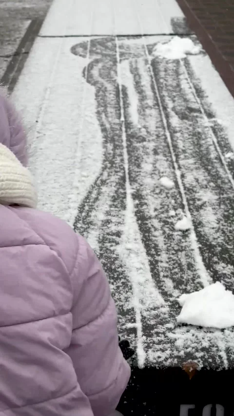 Child in winter clothes clearing snow from bench in snowy park Stock Footage 324848021