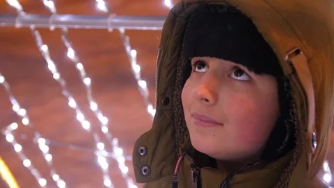 Child in winter warm clothes on the background of twinkling lights Stock Footage 105988297