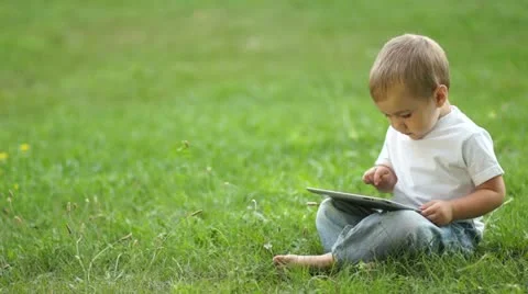 Child working with the Tablet PC sitting on the grass Video stock 11408152