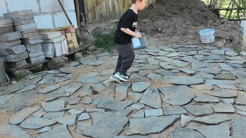 Child works on stone path in backyard during sunny day Stock Footage 340357190