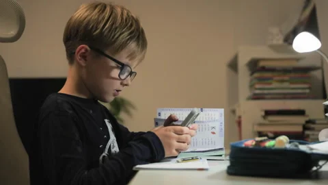 A child at a write table picks up a phone and responds to a text message Stock Footage 322517035