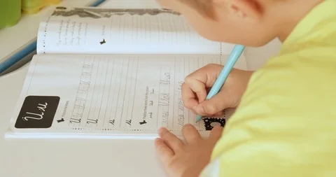 Child writes the letters in school notebook. Schoolboy is doing  homework at  Stock Footage 121062231