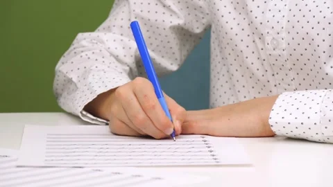 A child writes with a pen while sitting at a desk with a speckled plan. A Stock Footage 261267387