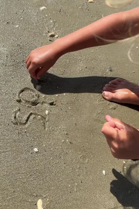 Child writing by hand phrase SPF and drawing heart in sand by sea Stock Footage 246504199