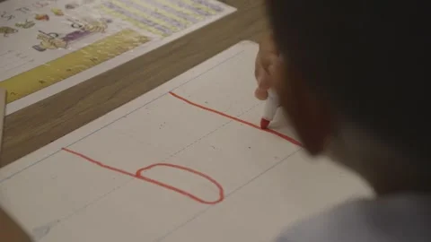 Child writing lowercase d with red marker on a small whiteboard 库存影片 304372735
