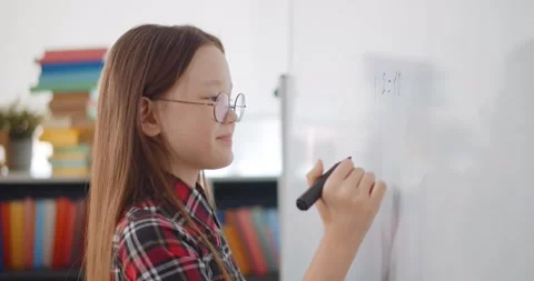 Child writing solution of mathematical operation on board in classroom. Stock Footage 153419618
