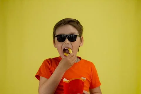 A child on a yellow background eats a large handful of french fries. Isolated Stock Photos